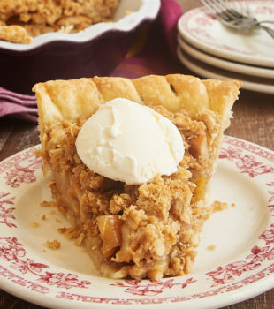 Slice of Apple Crumb Pie topped with a scoop of vanilla ice cream on a red floral-trimmed plate