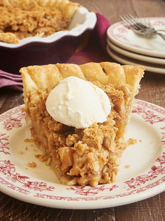 Slice of Apple Crumb Pie topped with a scoop of vanilla ice cream on a red floral-trimmed plate