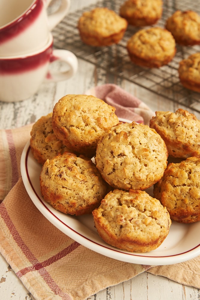 Oat Muffins with Nuts and Seeds on a white plate with more muffins and coffee cups in the background