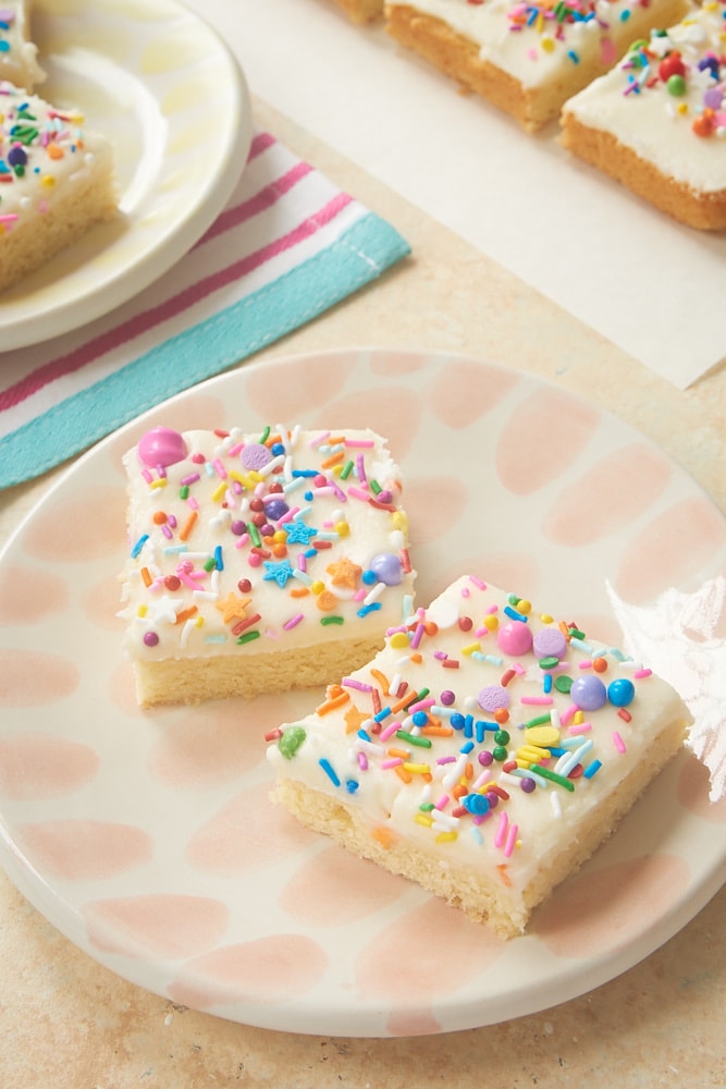 Two frosted sugar cookie bars on a white and pink plate.