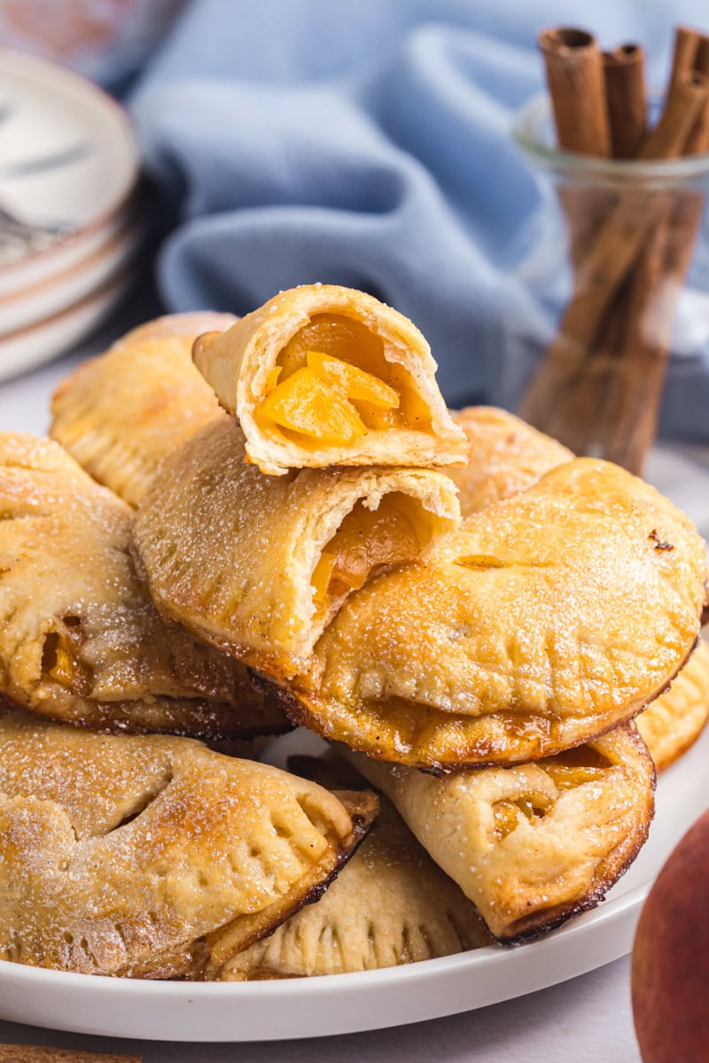 peach hand pies piled on a plate with the top pie cut in half to show the filling