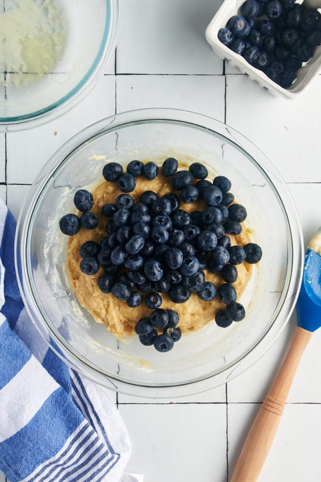 Fresh blueberries added into a bowl of batter.