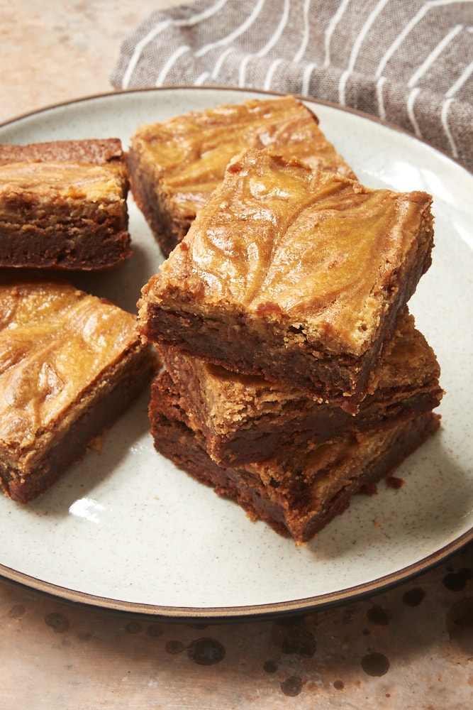 Cookie Butter Cheesecake Brownies stacked on a white and brown speckled plate