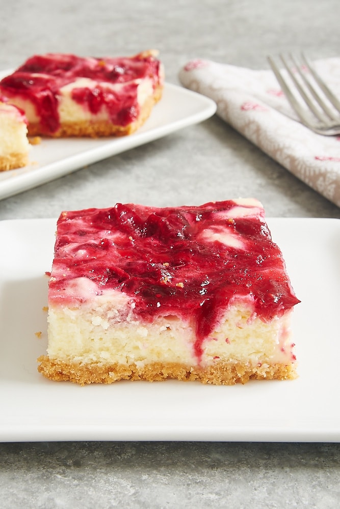 Cranberry White Chocolate Cheesecake Bars served on square white plates