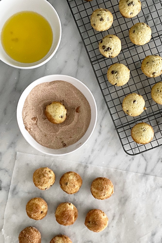 Mini Chocolate Chip Doughnut Muffins being dipped into butter and cinnamon-sugar