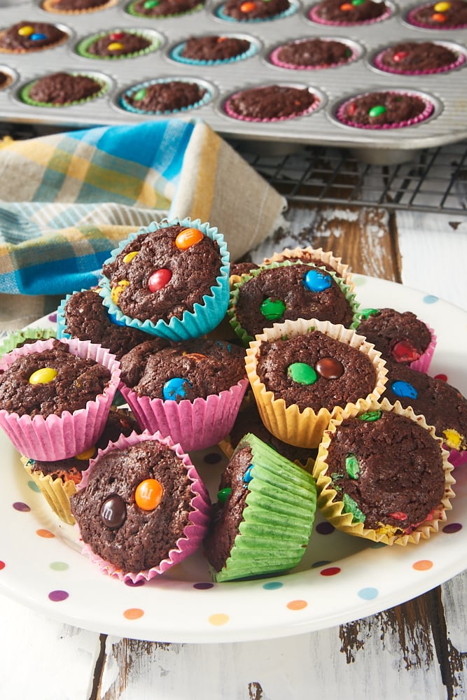 a pile of M&M Brownie Bites on a plate with more brownies in a pan in the background
