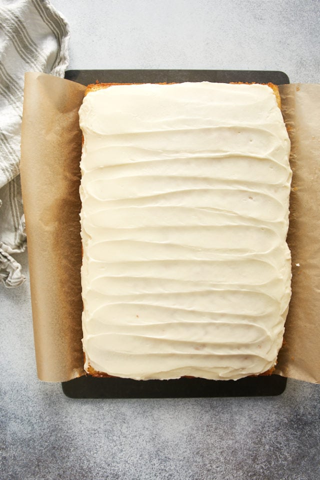 Overhead view of frosted cake in parchment-lined baking pan