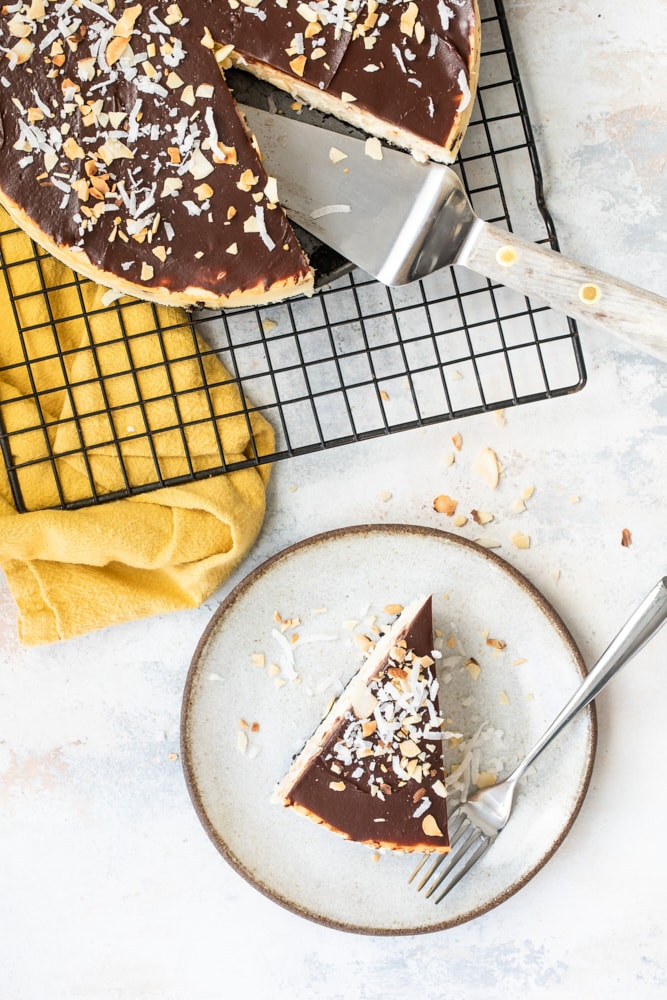 overhead view of a slice of  Chocolate Coconut Almond Cheesecake on a beige plate and the remaining cheesecake on a wire rack