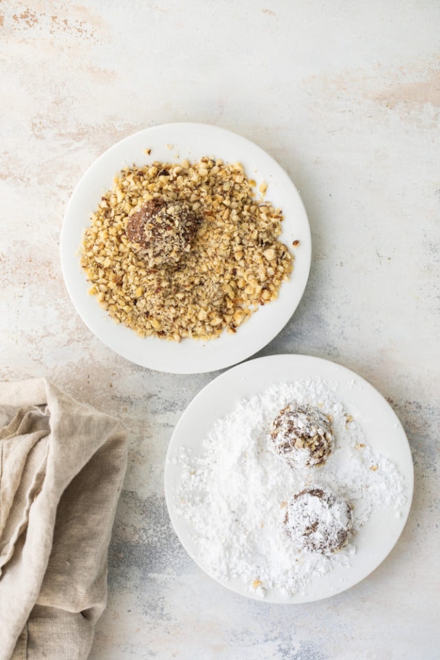 Hazelnut crinkle cookies dough being rolled in chopped hazelnuts and confectioners' sugar.