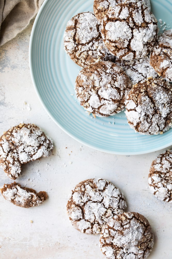 Overhead view of hazelnut crinkle cookies on a blue plate and a light beige surface.