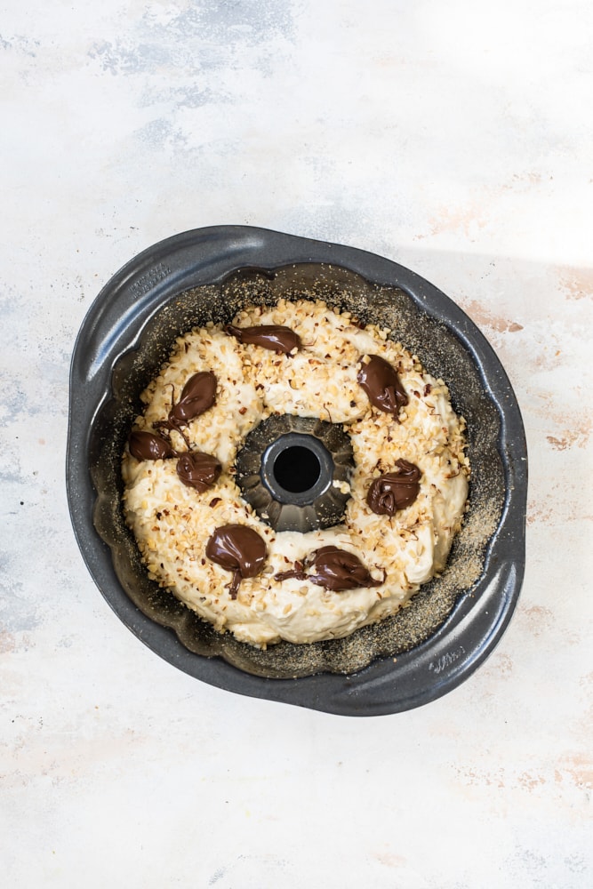 Overhead view of Nutella dropped on bundt cake batter in pan