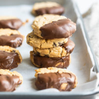Chocolate-Dipped Peanut Butter Meltaway Cookies stacked on a parchment-lined baking sheet