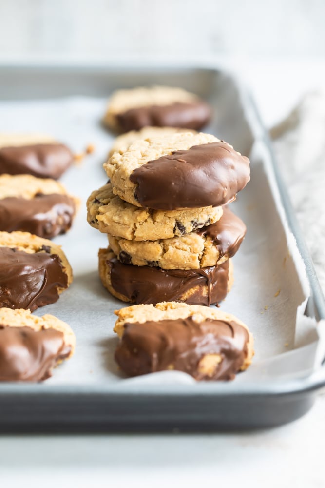 Chocolate-Dipped Peanut Butter Meltaway Cookies stacked on a parchment-lined baking sheet