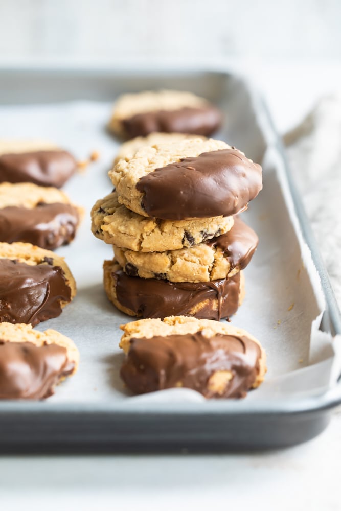 Chocolate-dipped peanut butter meltaway cookies stacked on a parchment-lined baking sheet.