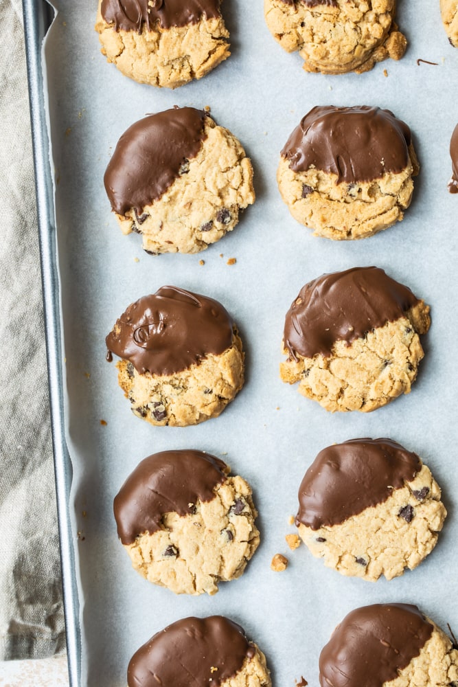 Overhead view of chocolate-dipped peanut butter meltaway cookies on a parchment-lined baking pan.