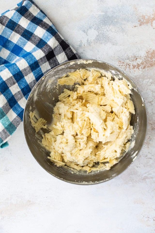 overhead view of potato chips added to cookie dough in a metal mixing bowl