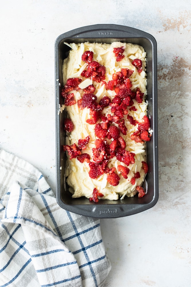 Overhead view of almond loaf in pan with raspberries scattered over batter