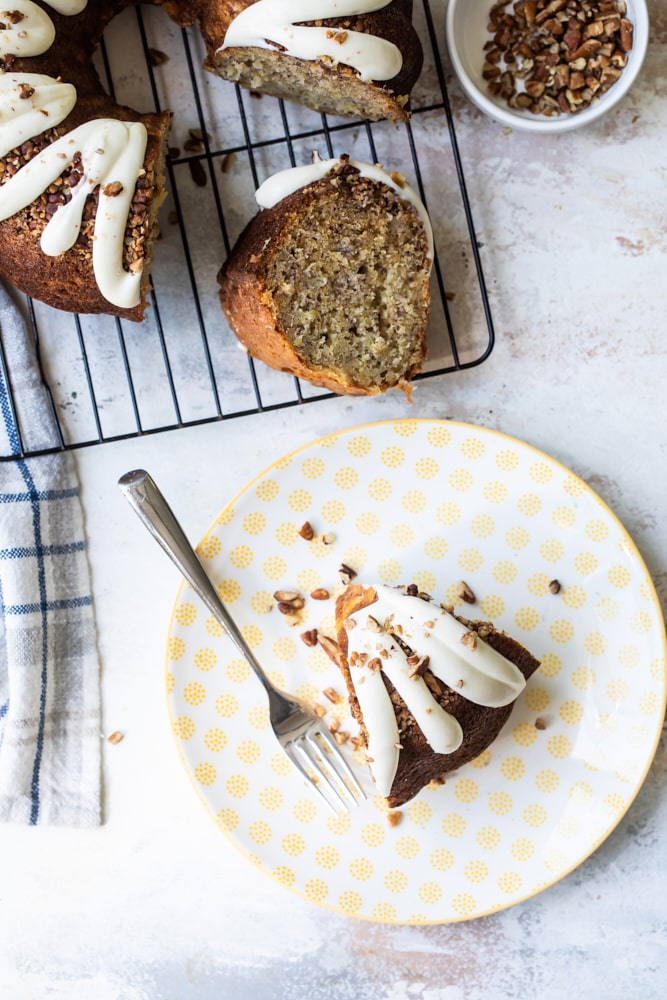 overhead view of a slice of Hummingbird Bundt Cake on a yellow and white plate with the remaining cake on a wire rack