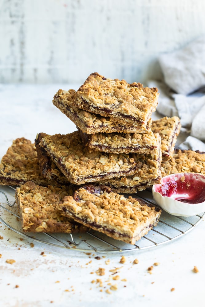 Raspberry bars stacked on wire rack with small bowl of jam