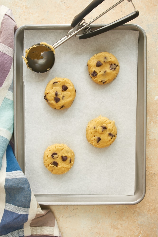 Overhead view of chocolate chip cookie dough on a parchment-lined baking sheet next to a cookie scoop.