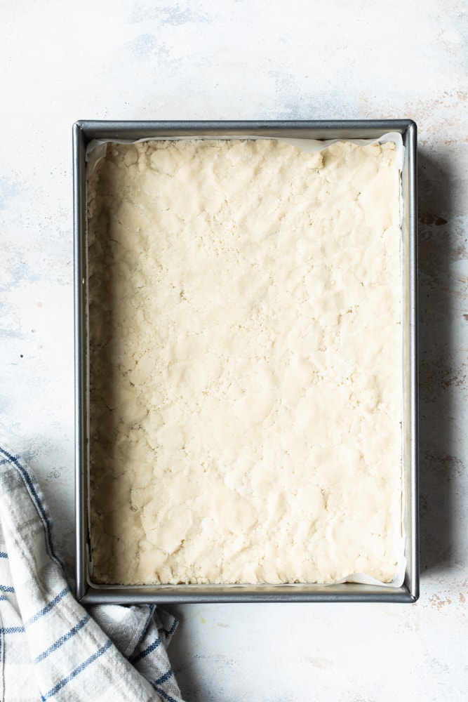 Overhead view of shortbread crust dough in a metal baking pan.