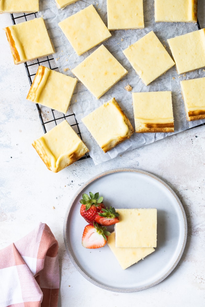 Overhead view of cheesecake bars on wire rack and stacked on a plate with strawberries