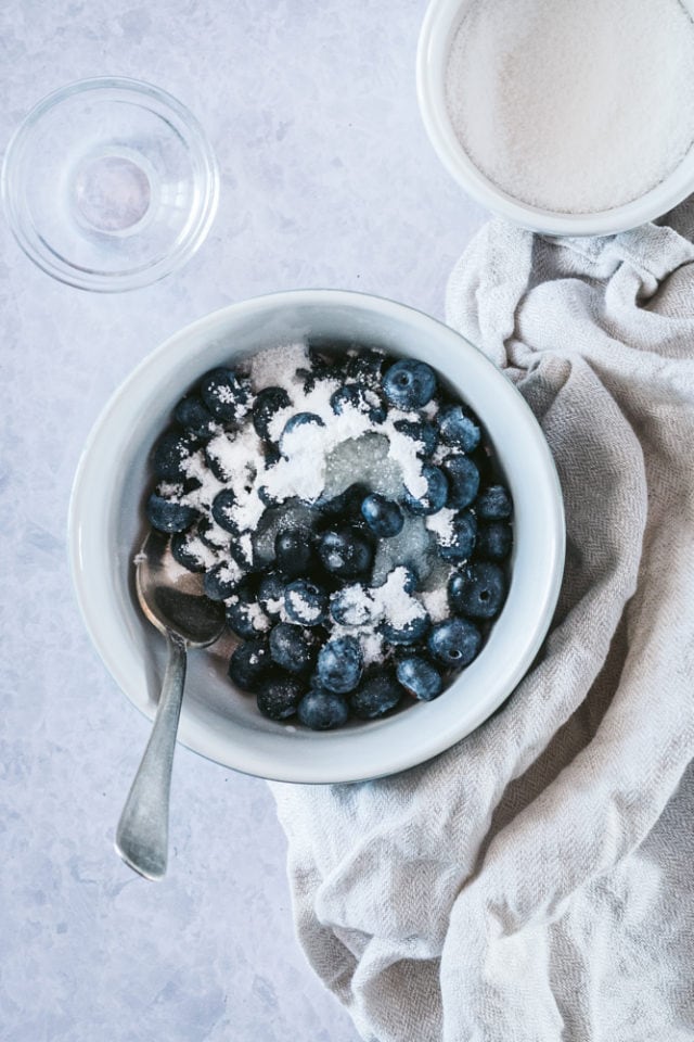 Blueberries, sugar, and lemon juice in a white bowl.
