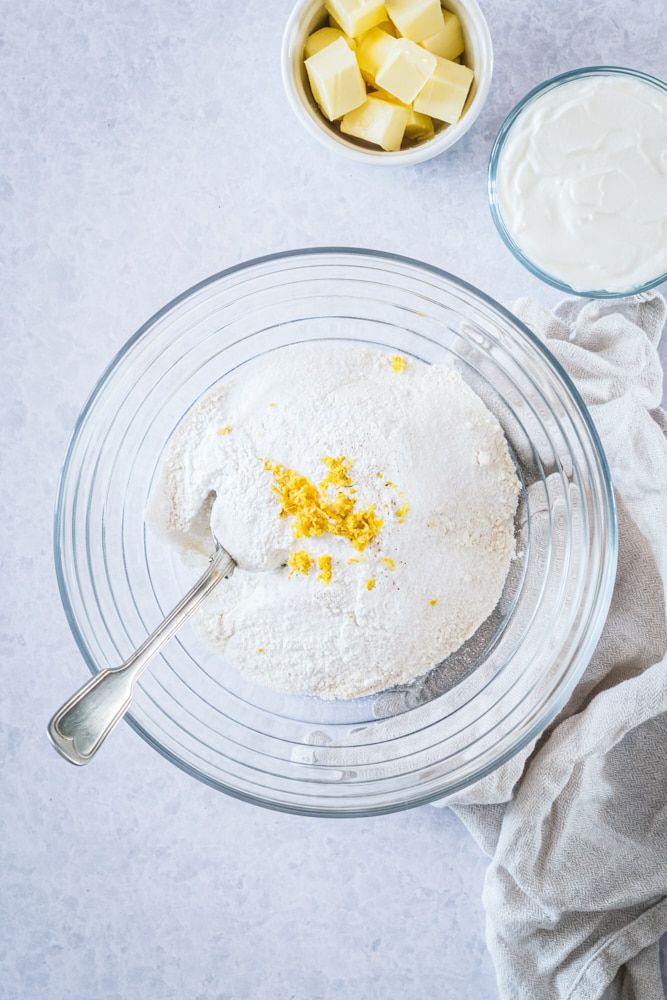 overhead view of sugar, flour, baking powder, lemon zest, and salt in a glass mixing bowl