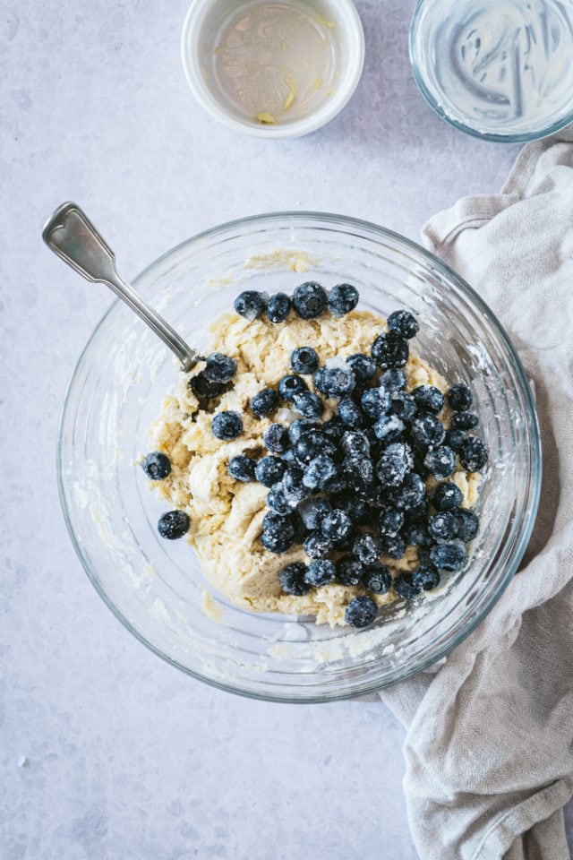 Overhead view of blueberries added to dough in a glass mixing bowl.