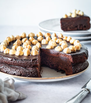 chocolate hazelnut cake on a serving plate with a slice removed to show the fudgy interior