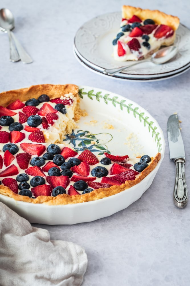 partially cut Fresh Berry Tart in a white tart pan