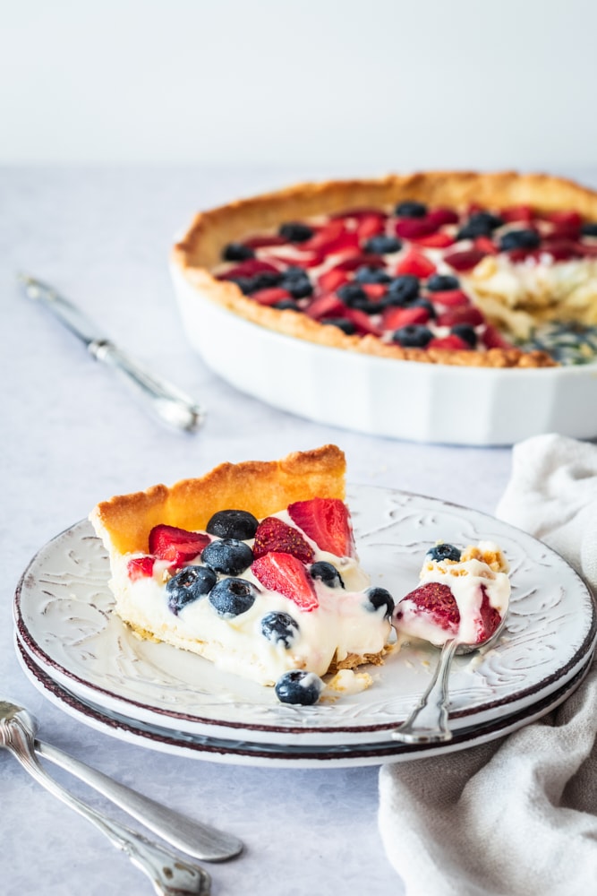 Slice of fresh berry tart on dessert plate with spoon