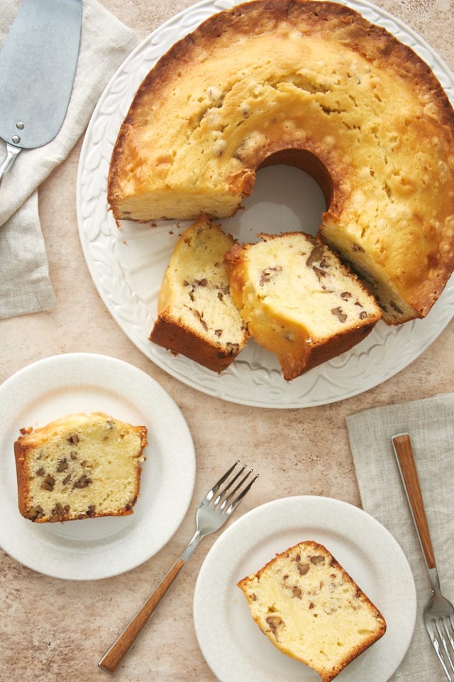 overhead view of slices of cream cheese pound cake on white plates and the remaining cake on a white cake plate