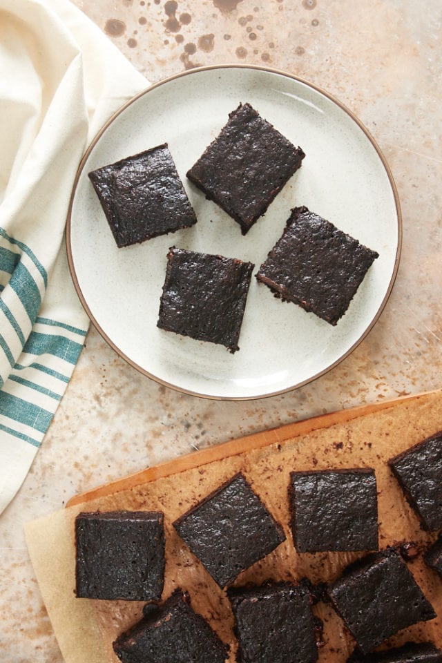 overhead view of Double Chocolate Zucchini Brownies on a beige plate and a wooden cutting board