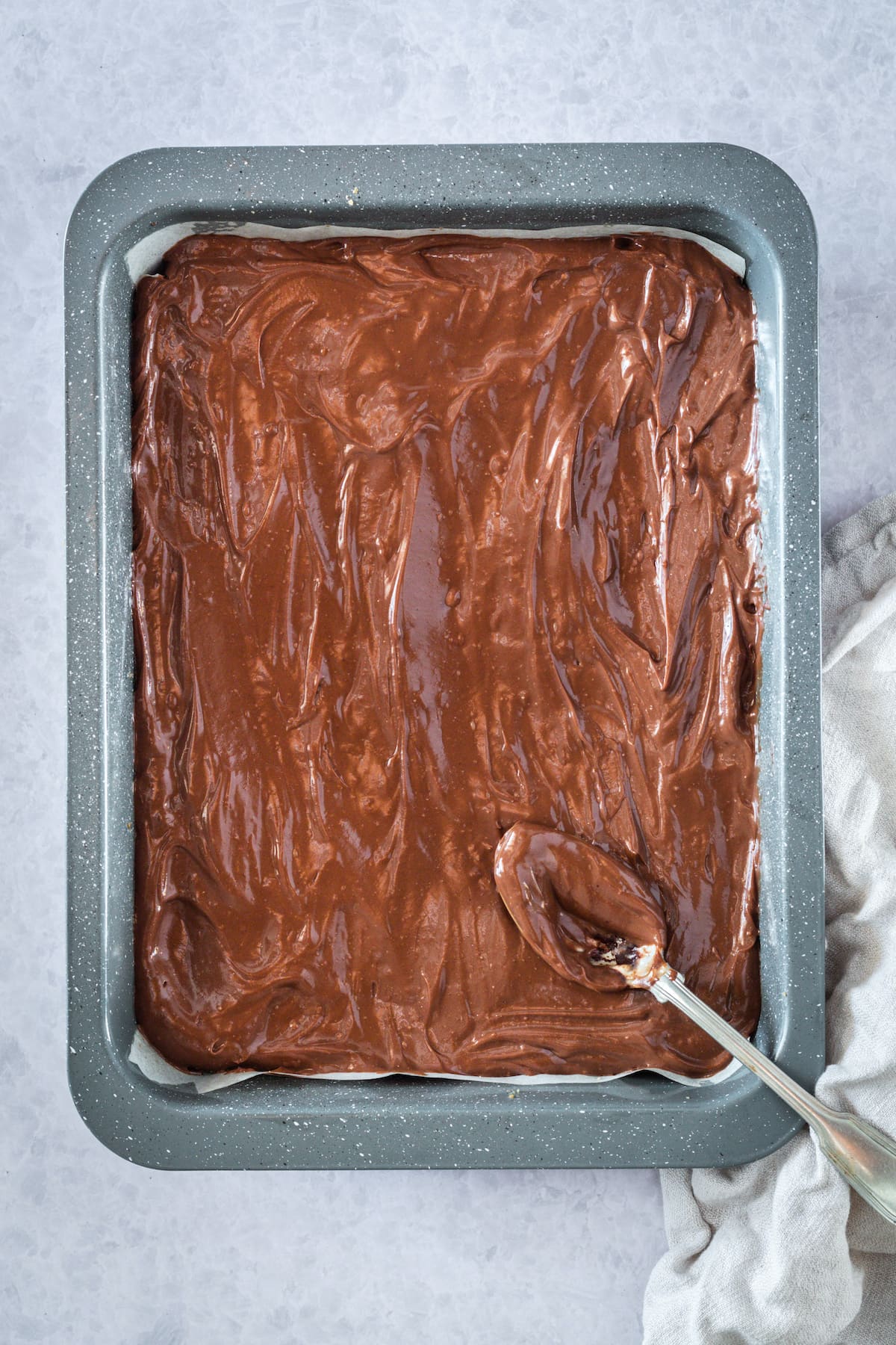 spreading a chocoalte cheesecake layer into a baking dish with a spoon