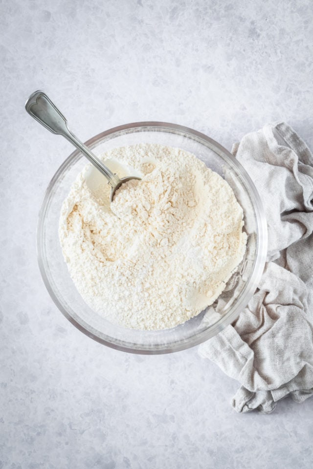 overhead view of flour, baking powder, baking soda, and salt in a glass mixing bowl