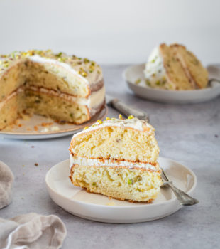 Two plated slices of Pistachio Cake with remaining cake in background