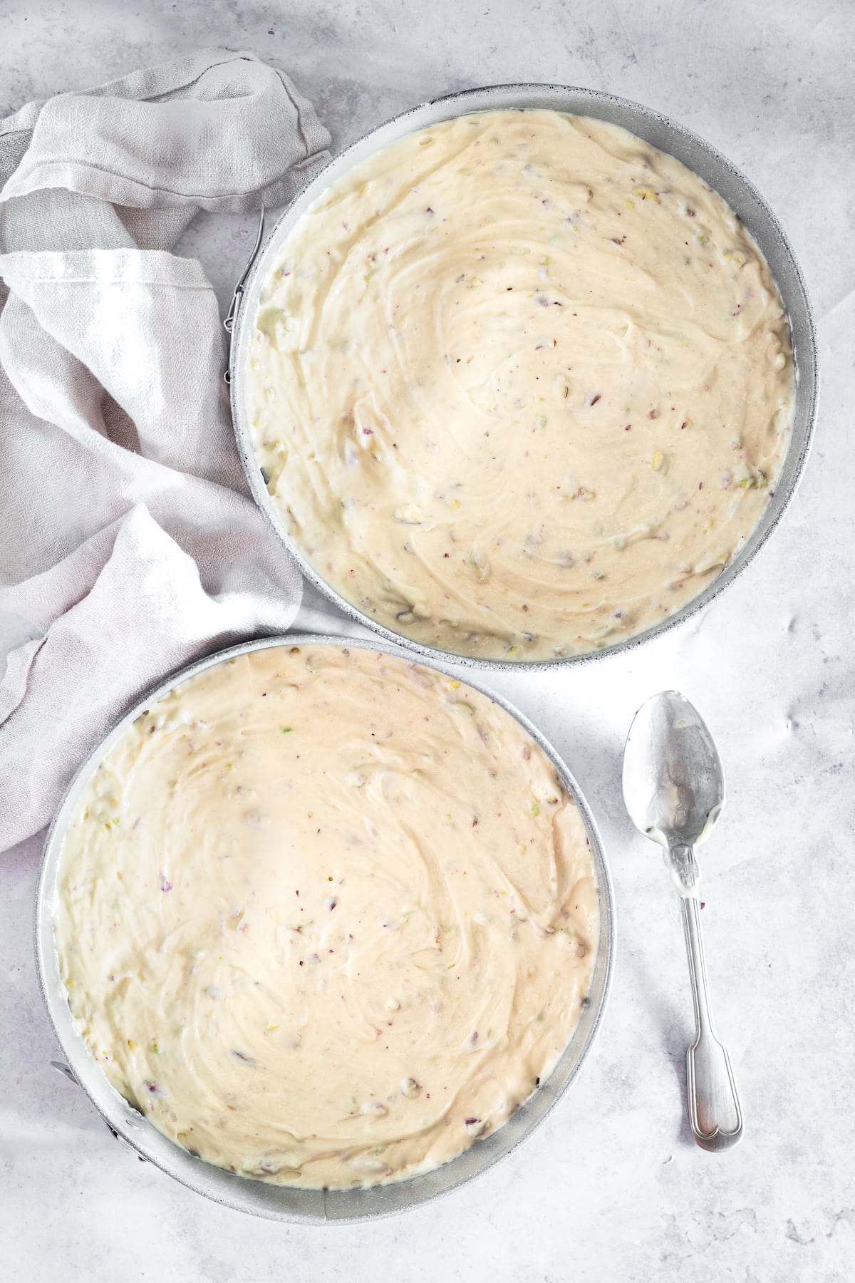 Overhead shot of pistachio cake batter in two round cake pans with spoon