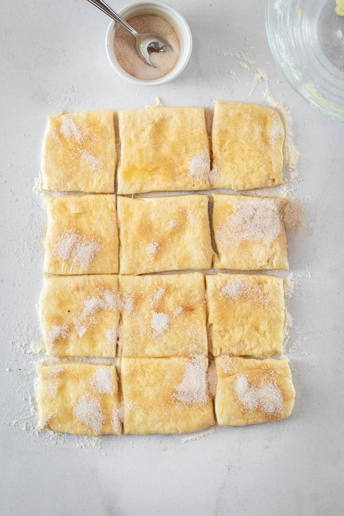 Overhead shot of biscuit dough cut into 12 pieces and dusted with cinnamon sugar, ready for baking