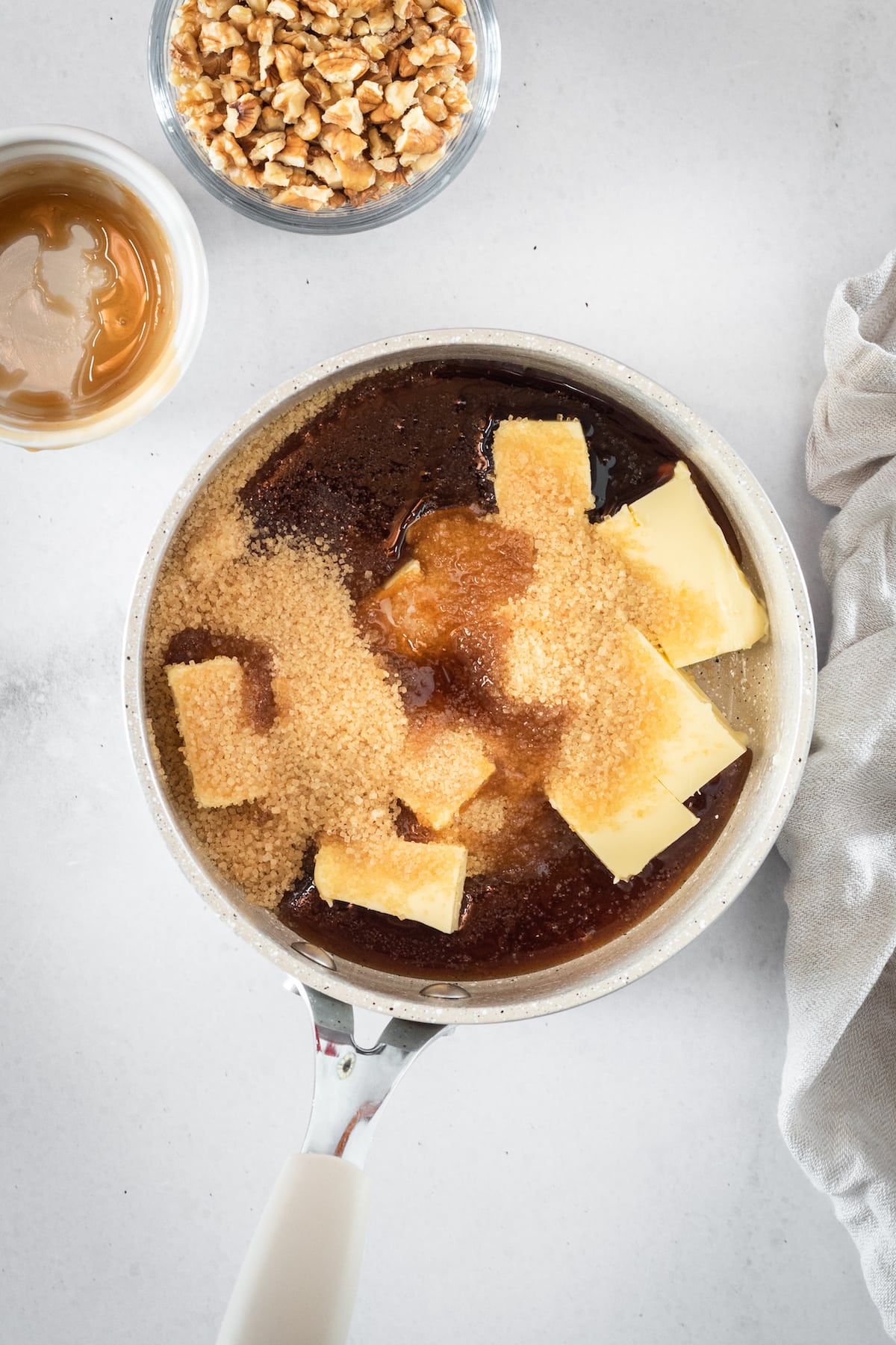 Overhead shot of butter and brown sugar being added to saucepan with caramel mixture