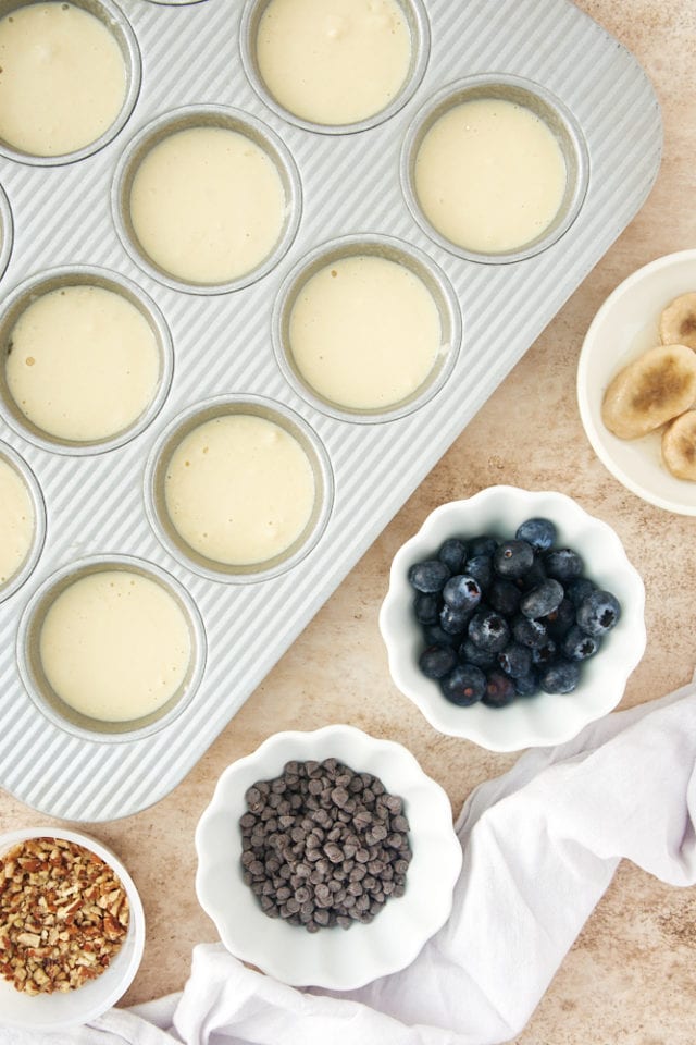 pancake batter in a muffin pan with bowls of various toppings