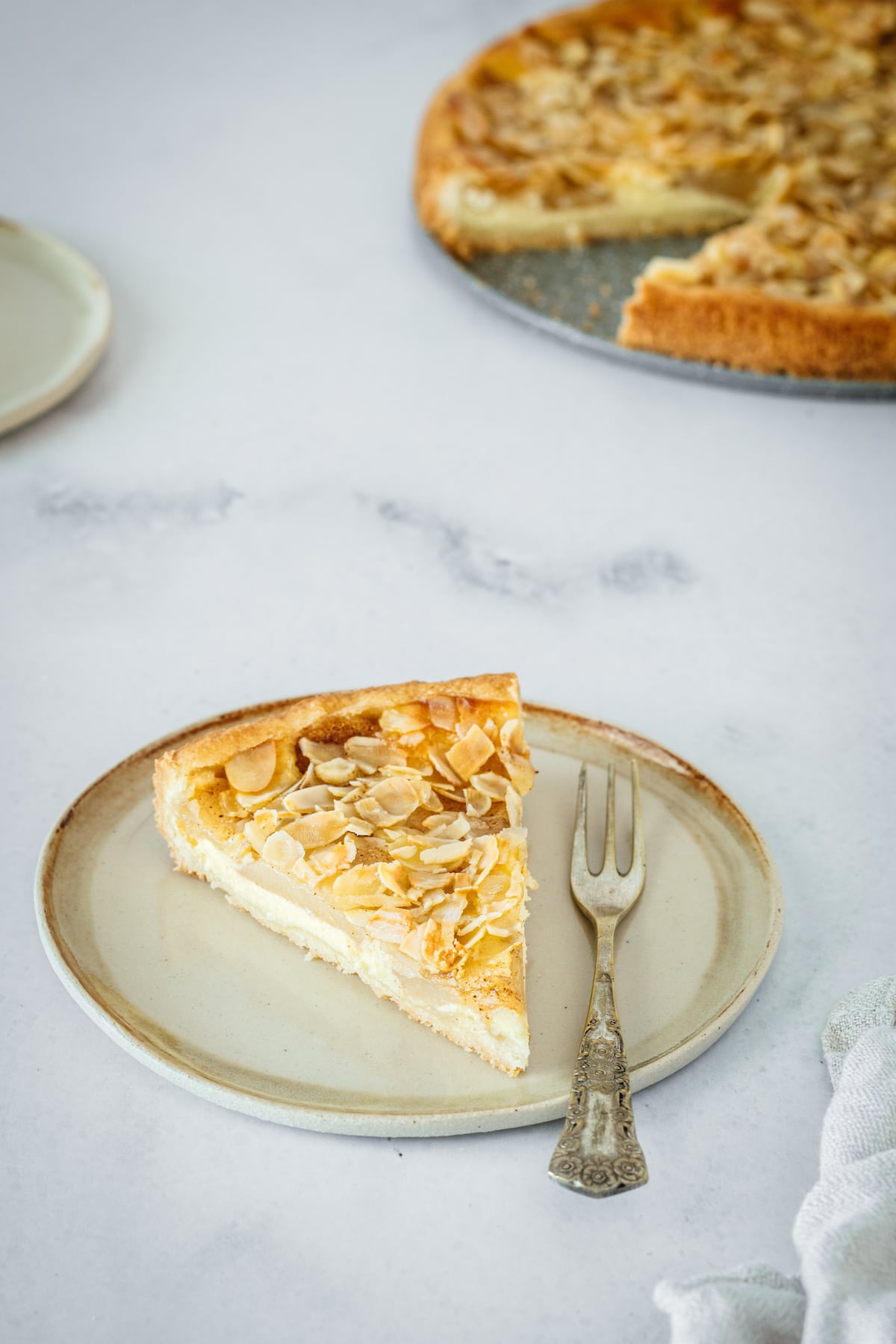 Overhead shot of pear tart slice on plate with the rest of the tart in the background