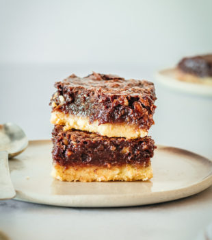 Two chocolate pecan pie bars stacked on plate