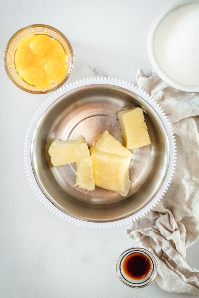 Overhead shot of butter in mixing bowl and bowls with egg yolks, flour, and vanilla