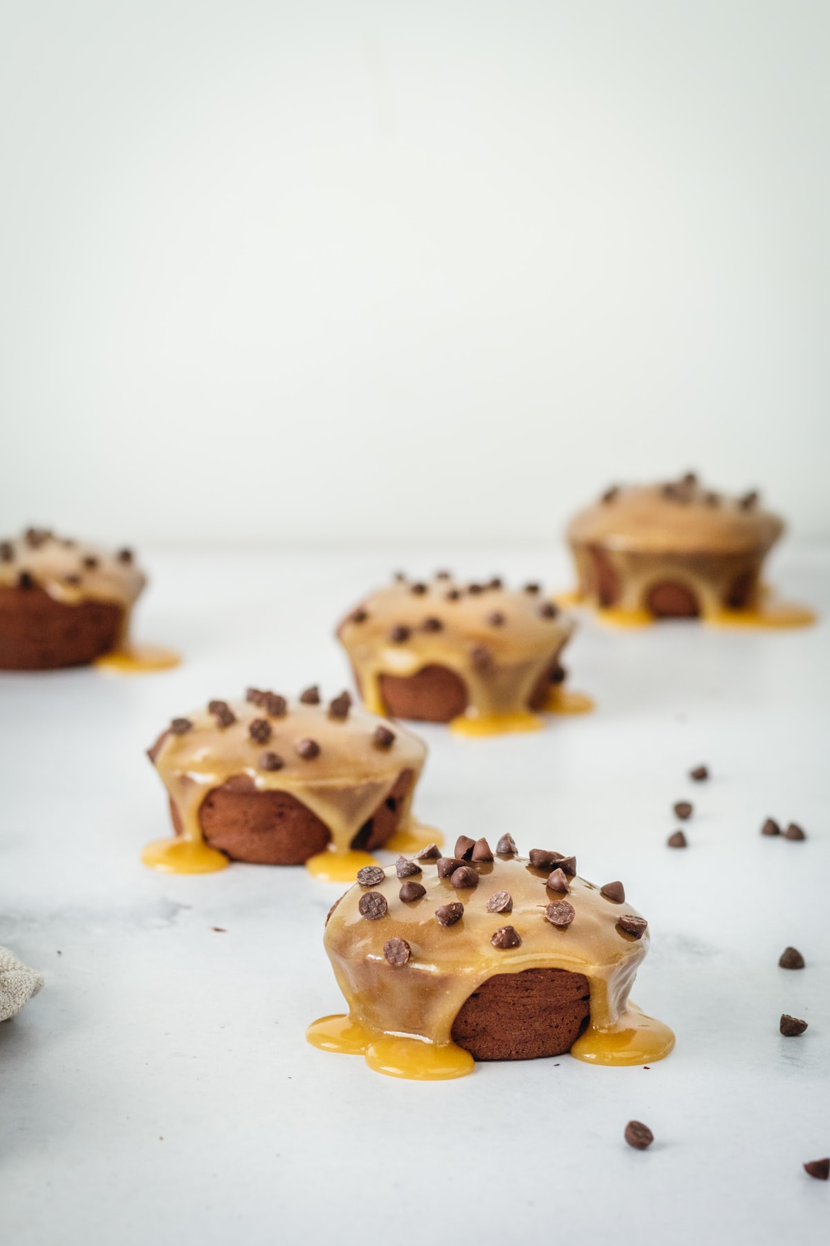 Mini chocolate cakes on marble baking slab after being drizzled with butterscotch and chocolate chip topping