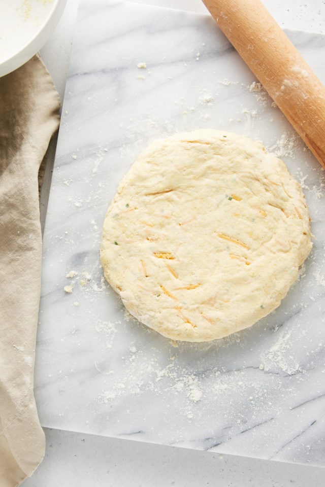 overhead view of rolled Cheddar and Chive Cornmeal Biscuits dough on a marble pastry dough