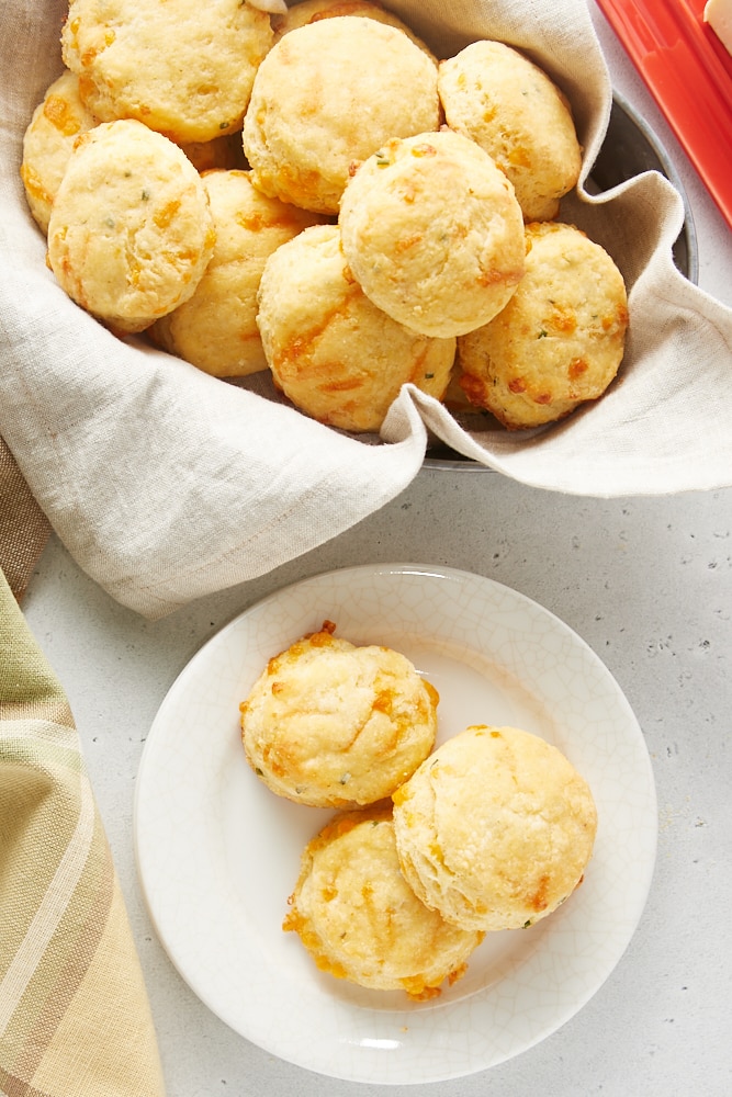 overhead view of Cheddar and Chive Cornmeal Biscuits on a white plate and in a towel-lined basket