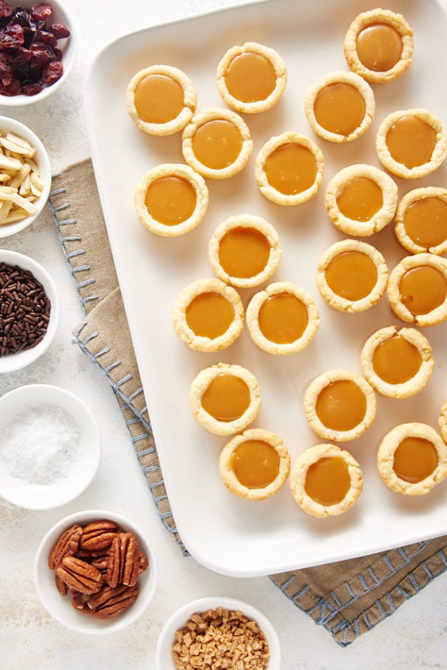 overhead view of Mini Caramel Tarts on a white serving tray with various toppings alongside