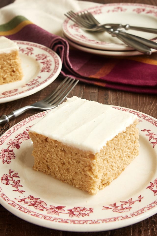a slice of Brown Sugar Spice Cake with Brown Butter Frosting served on a red floral-rimmed white plate