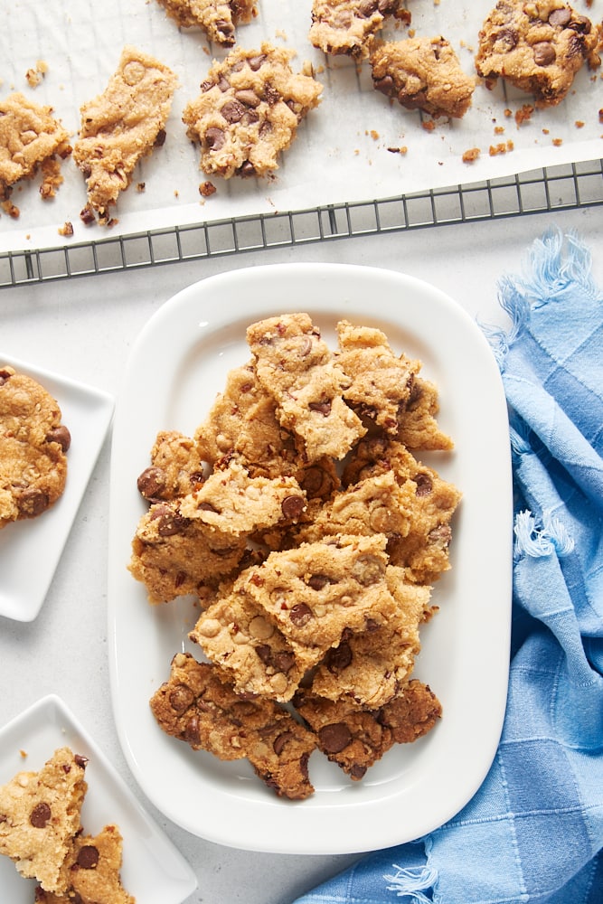 overhead view of Triple Chocolate Chip Cookie Brittle on a white tray, white plates, and a cooling rack